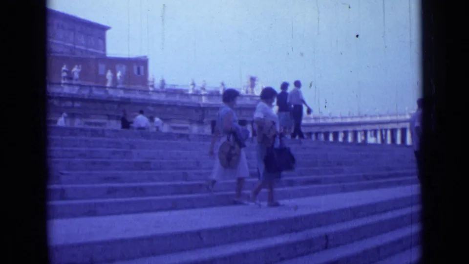 1962 Rome 8mm frame of tourists walking across a stepped public landmark, with terrace statues and large buildings in the background.