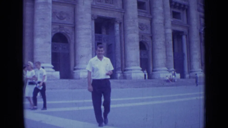 Near the end of the 1962 Rome clip, the man passes close to camera while the grand stone building and walkers remain behind him.