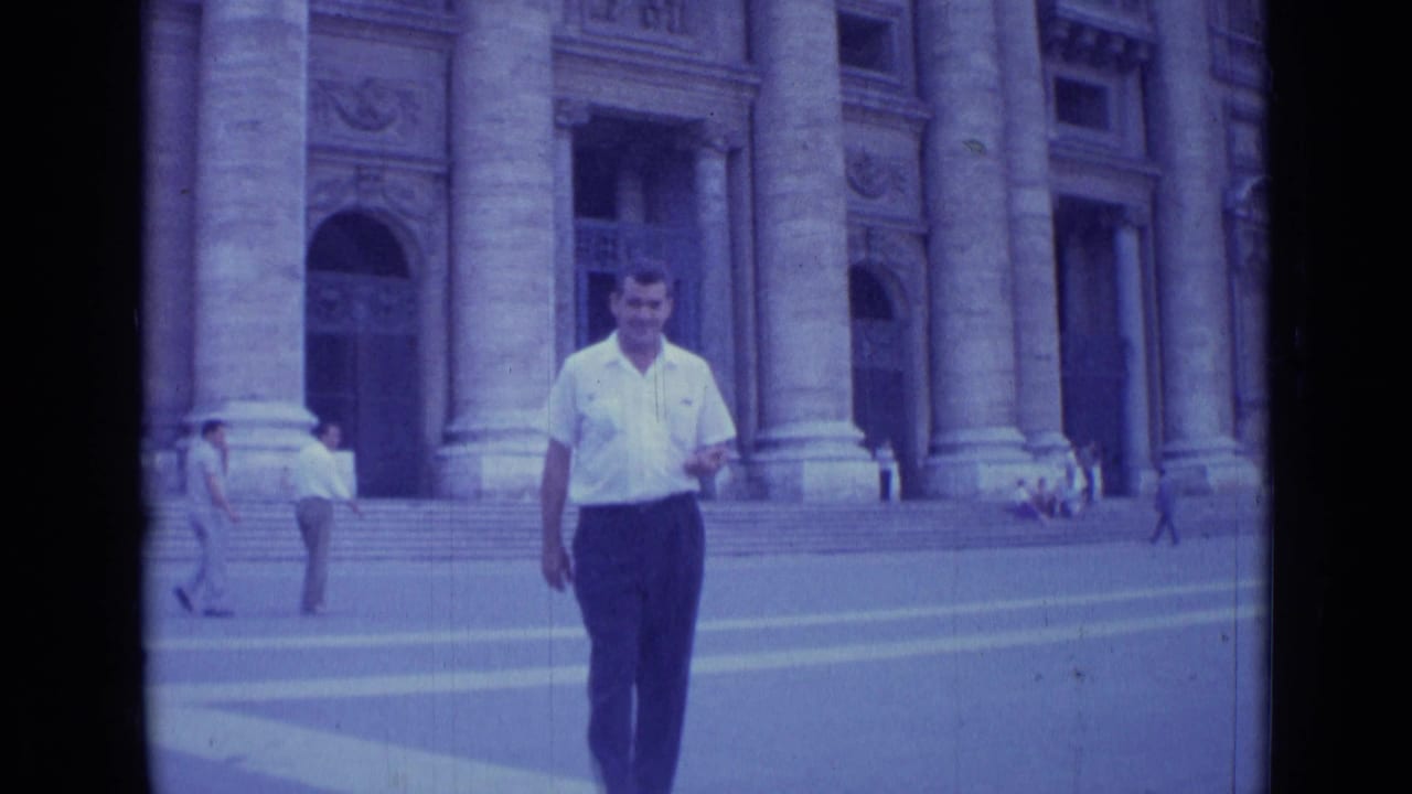 In Rome, Italy in 1962, a man in a white shirt walks toward the camera before a monumental columned facade.