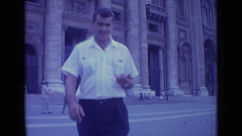 A closer 1962 Rome home-movie frame shows the man smiling and raising a hand before the monumental stone entrance.