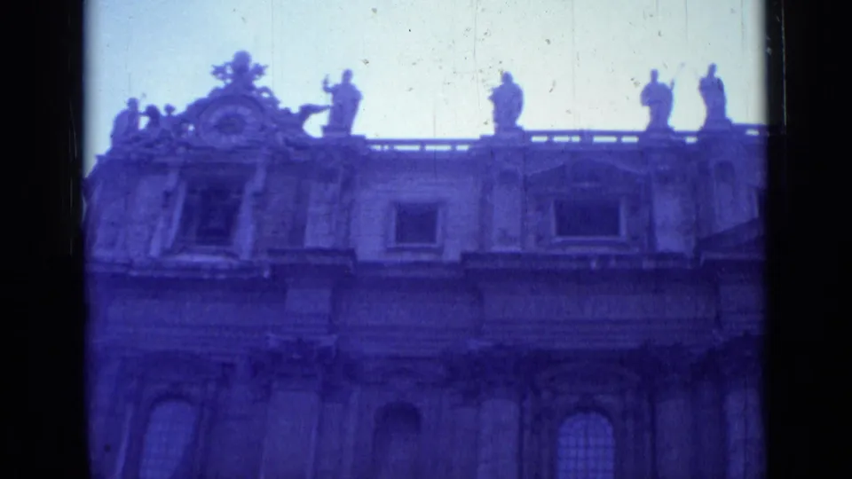 1962 Rome 8mm frame showing the upper facade of St. John Lateran with arched windows, roof statues, and blue-purple aged film color.