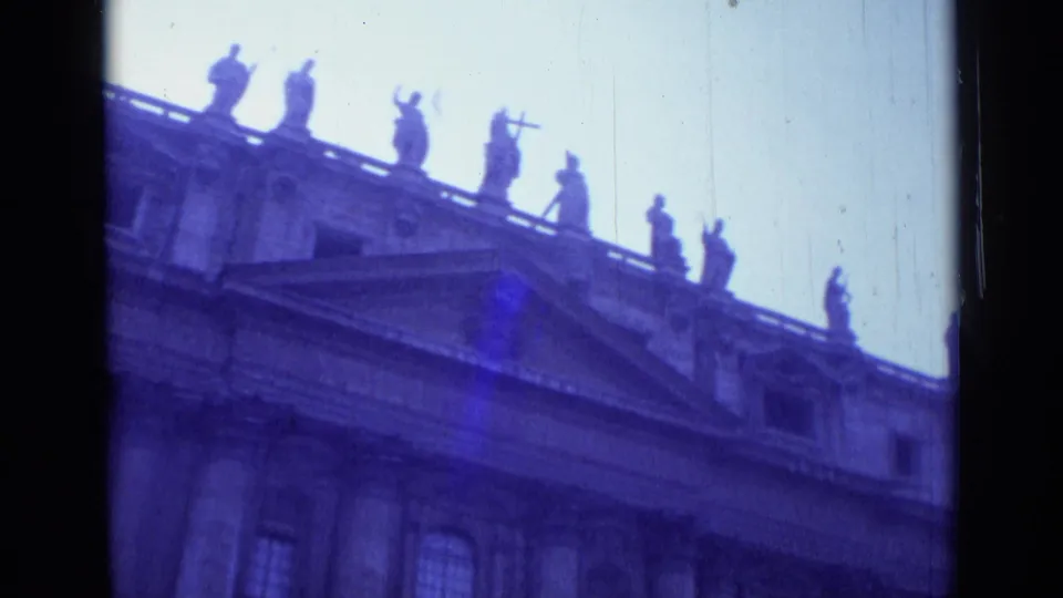 1962 Rome 8mm still showing St. John Lateran from below, with columns, arched windows, roofline statues, and visible film wear.