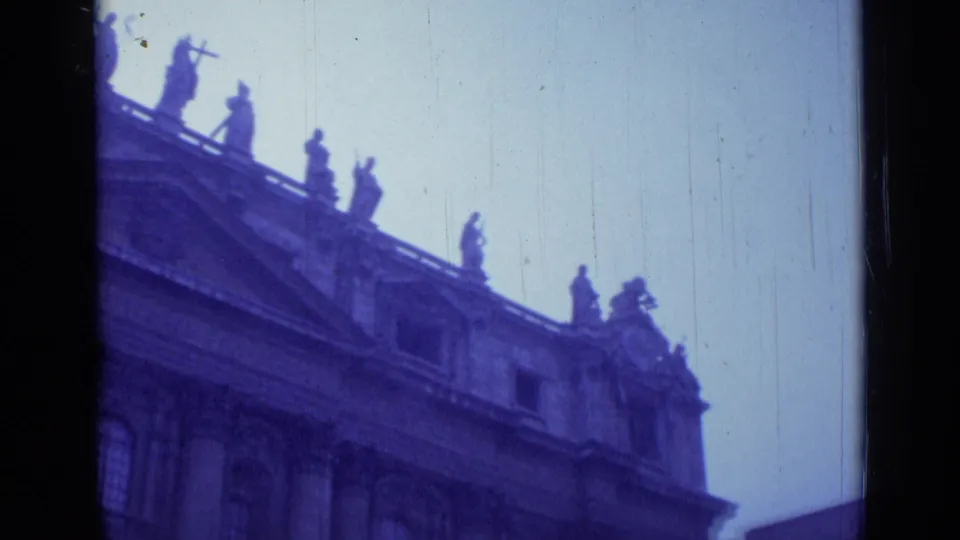 Final 1962 Rome frame of St. John Lateran's upper facade, with statues on the roofline, a pediment, soft focus, and blue-purple film tint.