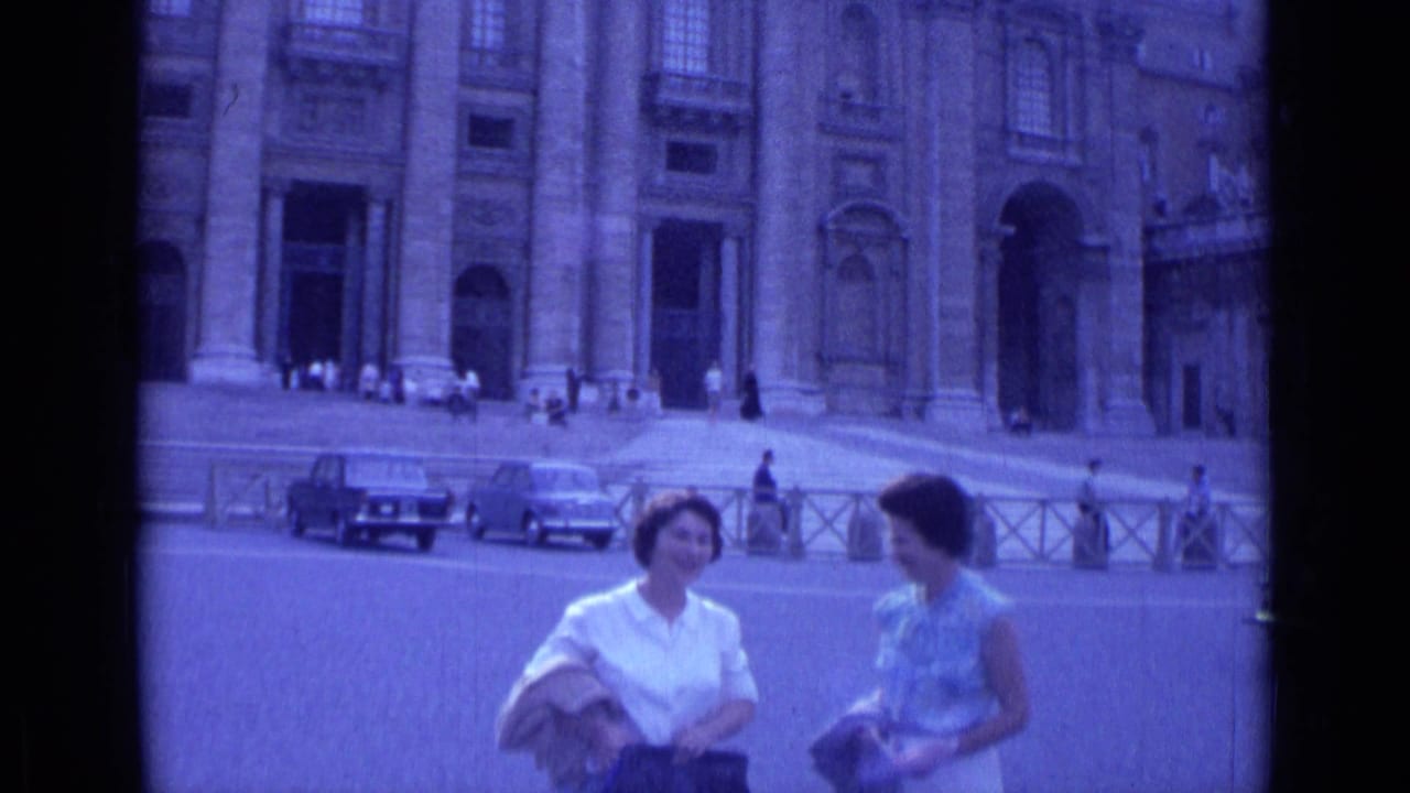 Two women talking in front of a large church facade with cars and pedestrians behind them.