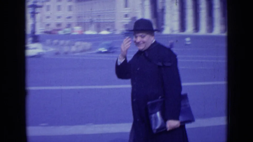 Close 1962 Rome frame of a man in a black hat and coat smiling and waving, with St. Peter's Square behind him.