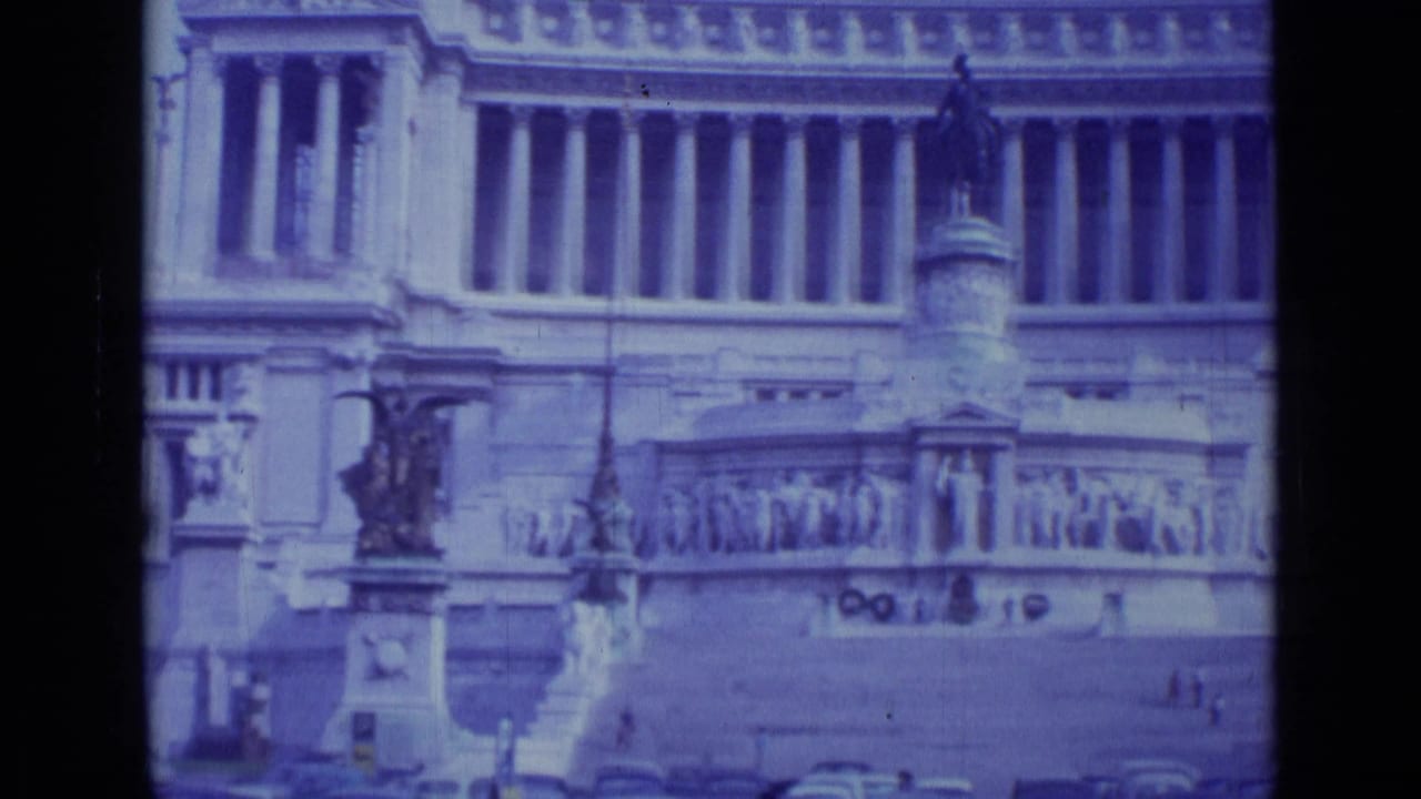 1962 Rome 8mm frame showing a monumental stone facade with columns, relief sculpture, steps, a statue, and tiny figures in the plaza.