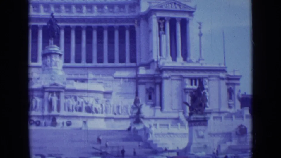 1962 Rome 8mm frame showing the right side of a monumental facade with columns, steps, an equestrian statue, and pale sky.