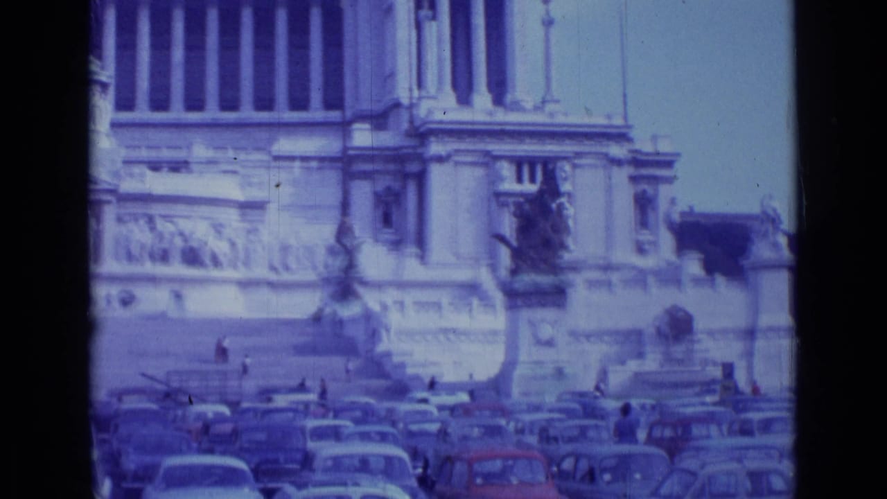 Distant monument facade behind rows of parked classic cars and dark 8mm frame edges.