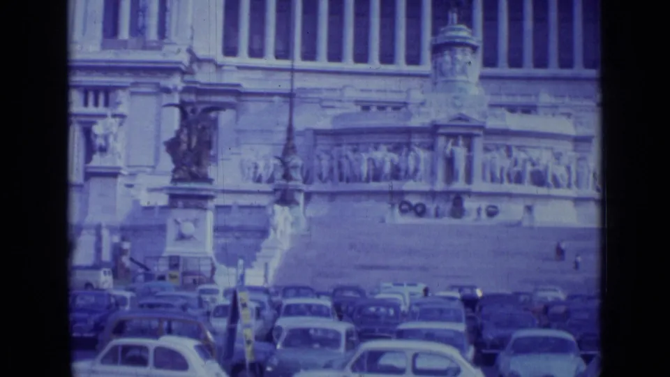 1962 Rome frame showing a statue, carved monument facade, and many compact cars under a blue-tinted 8mm look.