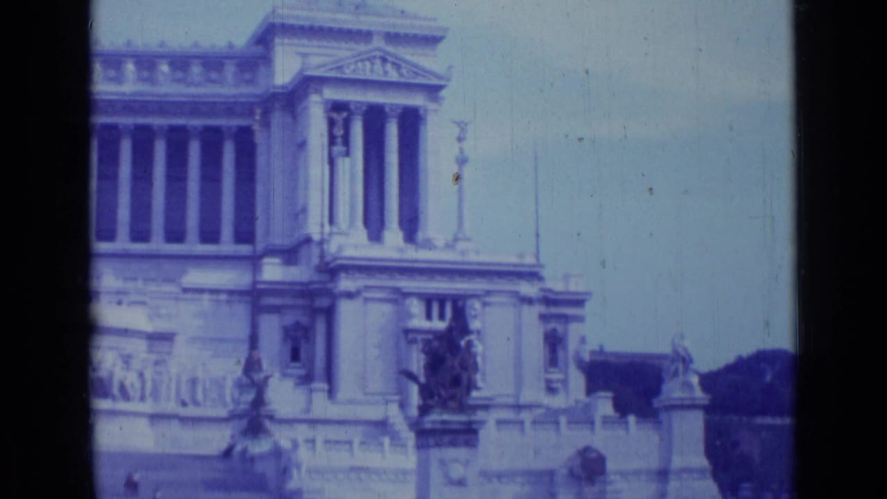Blue-tinted view of a monumental classical facade with columns, statues, and stone railings.