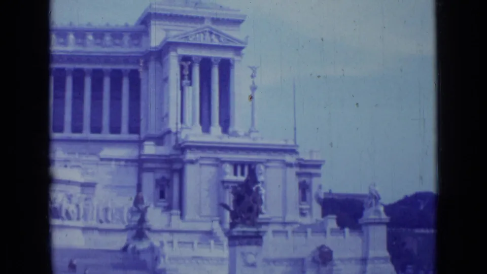 1962 Rome 8mm frame showing a blue-tinted monumental classical building facade with columns, sculpture, and stone railings.