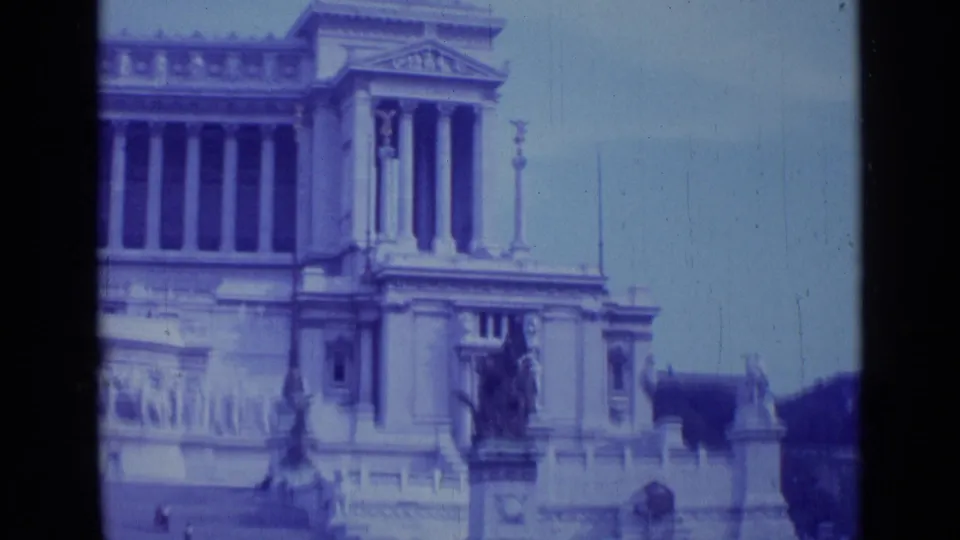 1962 Rome 8mm frame with the monumental facade held in view, showing columns, statuary, railings, and dark film borders.