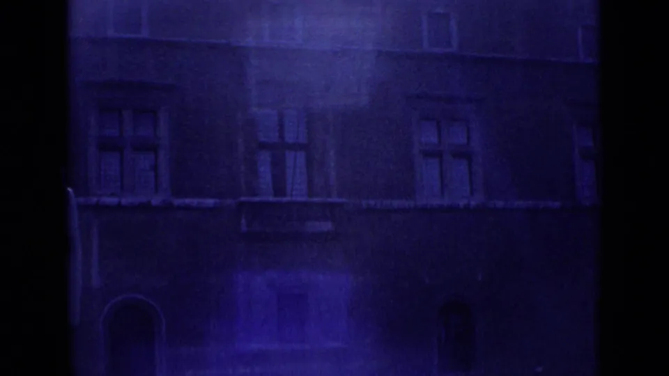 1962 Rome 8mm frame showing a darker blue-tinted city facade with rectangular windows, balconies, and arched ground-level openings.