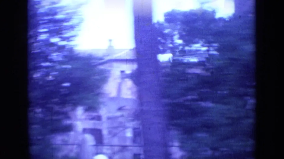 1962 Rome home-movie frame with handheld motion blur, trees, bright sky, and a tall architectural form in the distance.