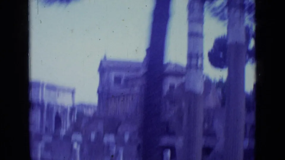 1962 Rome home-movie frame with a tree trunk in the foreground and blurred arches and old stone architecture beyond.