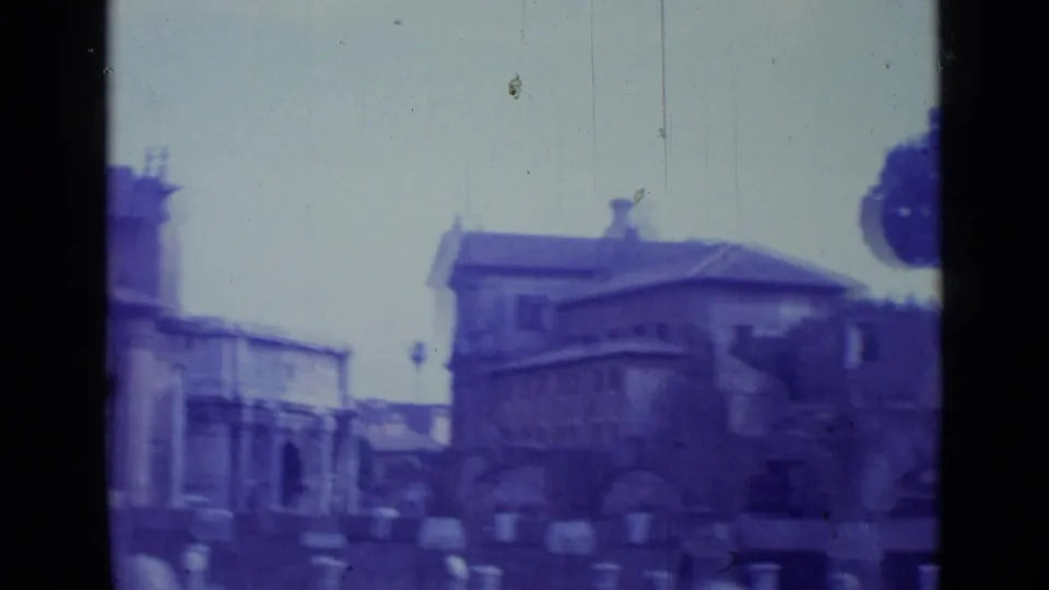 Purple-cast 1962 Rome home-movie frame showing stone buildings, a public overlook, and blurred historic structures.