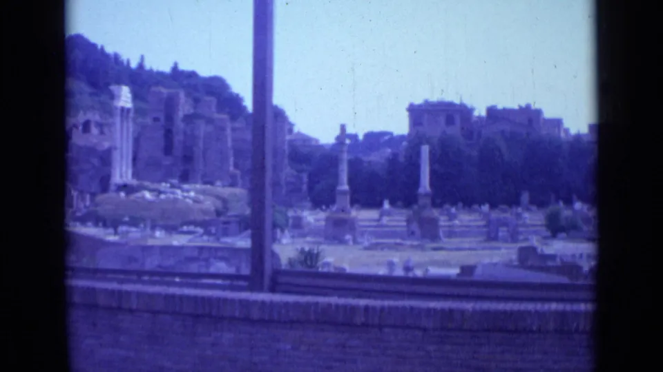 The final frame holds on Rome ruins, columns, trees, a low foreground wall, and distant urban buildings under a bright sky.