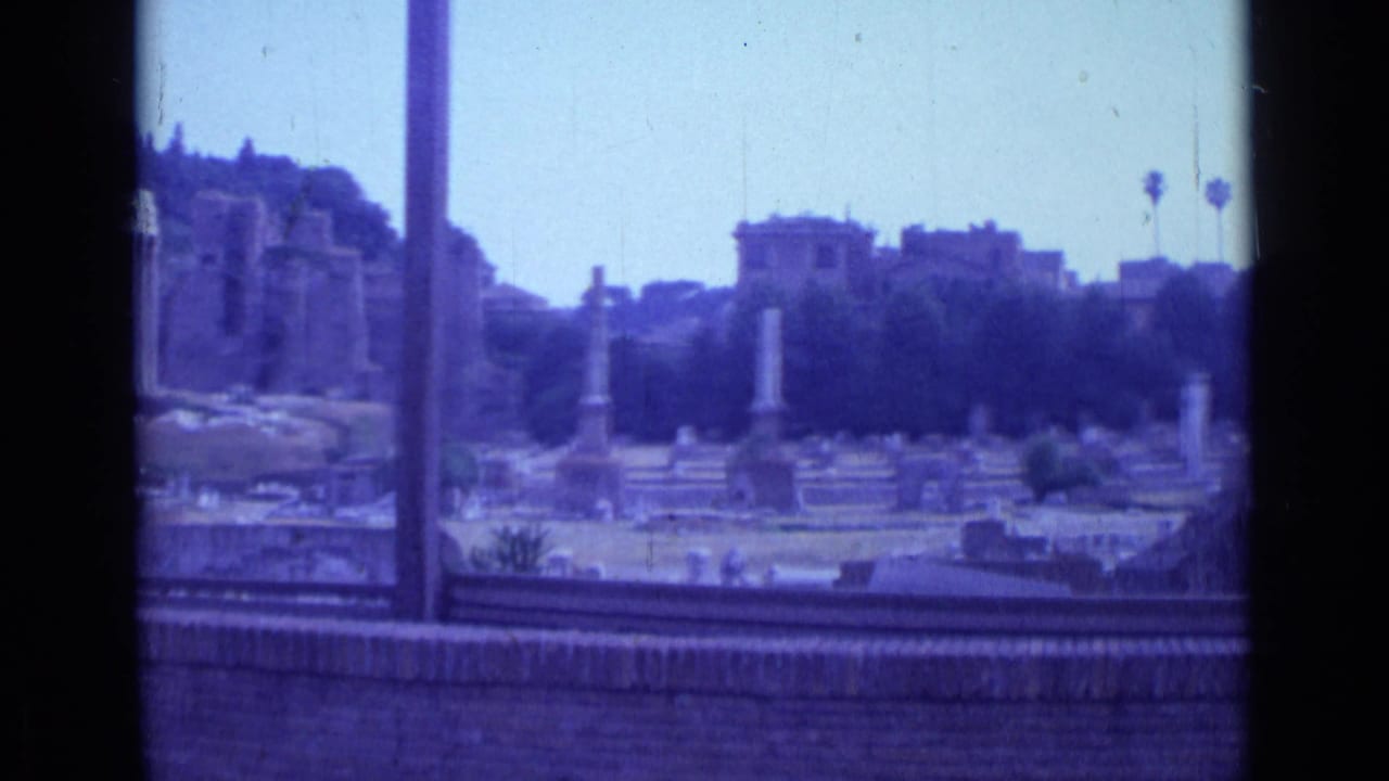 Window-framed view over tombs, columns, ruins, and distant buildings under a pale sky.