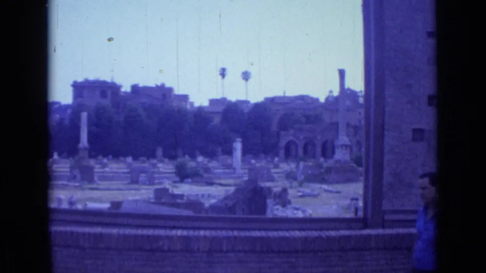 1962 Rome 8mm frame showing tombs, columns, ruins, and a partially visible man passing near the lower right edge.