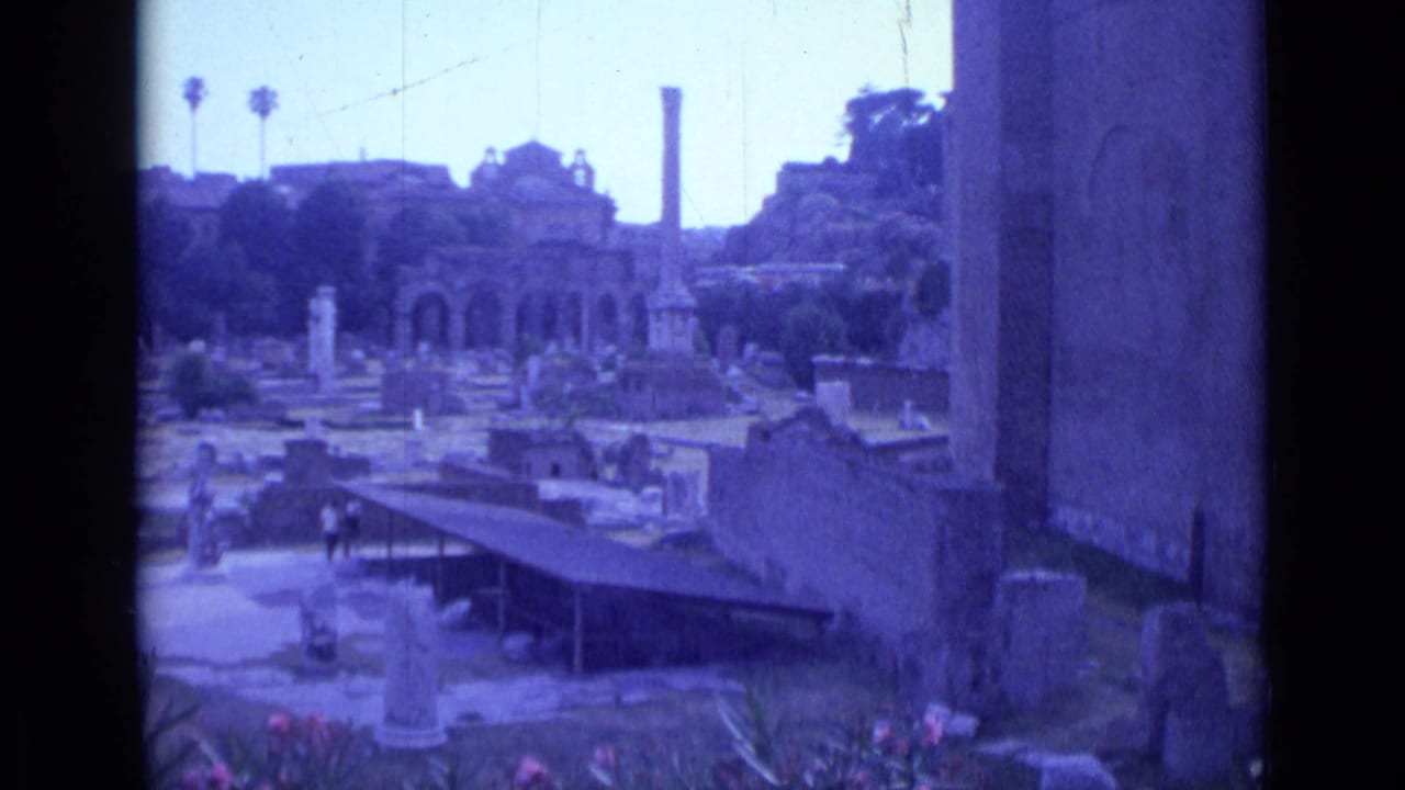 Wide view of a Rome street area with monuments, pedestrians and tall structures in the distance.