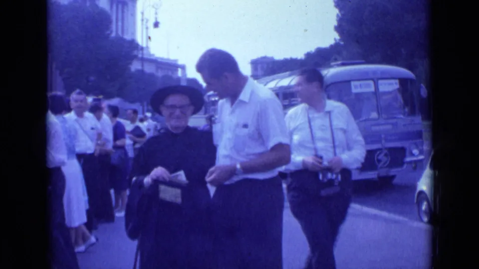 In 1962 Rome, a man in a white shirt faces a nun in a black habit holding a donation box, with pedestrians and a bus behind them.