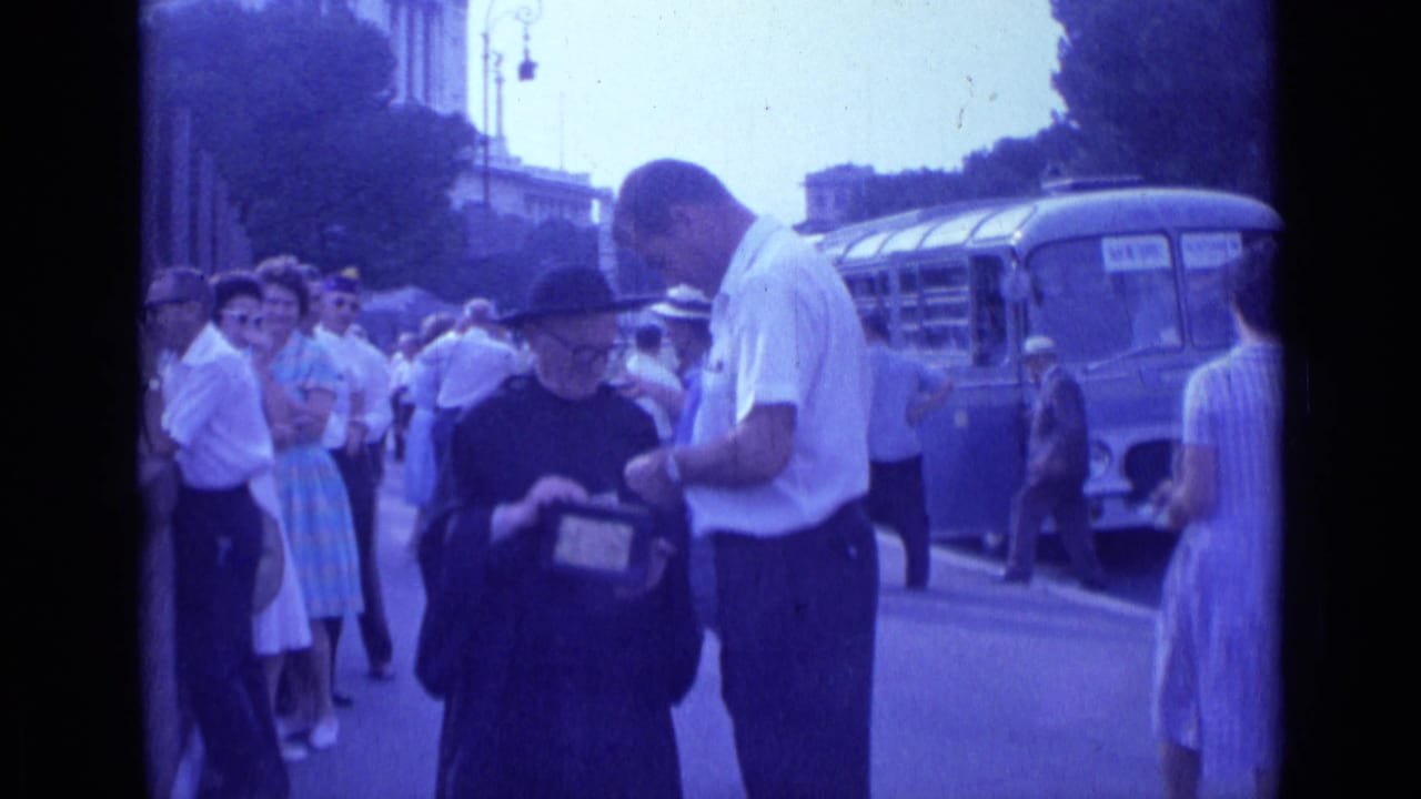 Man in a white shirt leans toward a robed figure holding a small box on a crowded street.