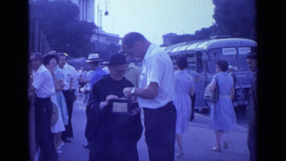 The Rome street scene shows pedestrians, a bus, and a man leaning over a robed figure who holds a small donation box.