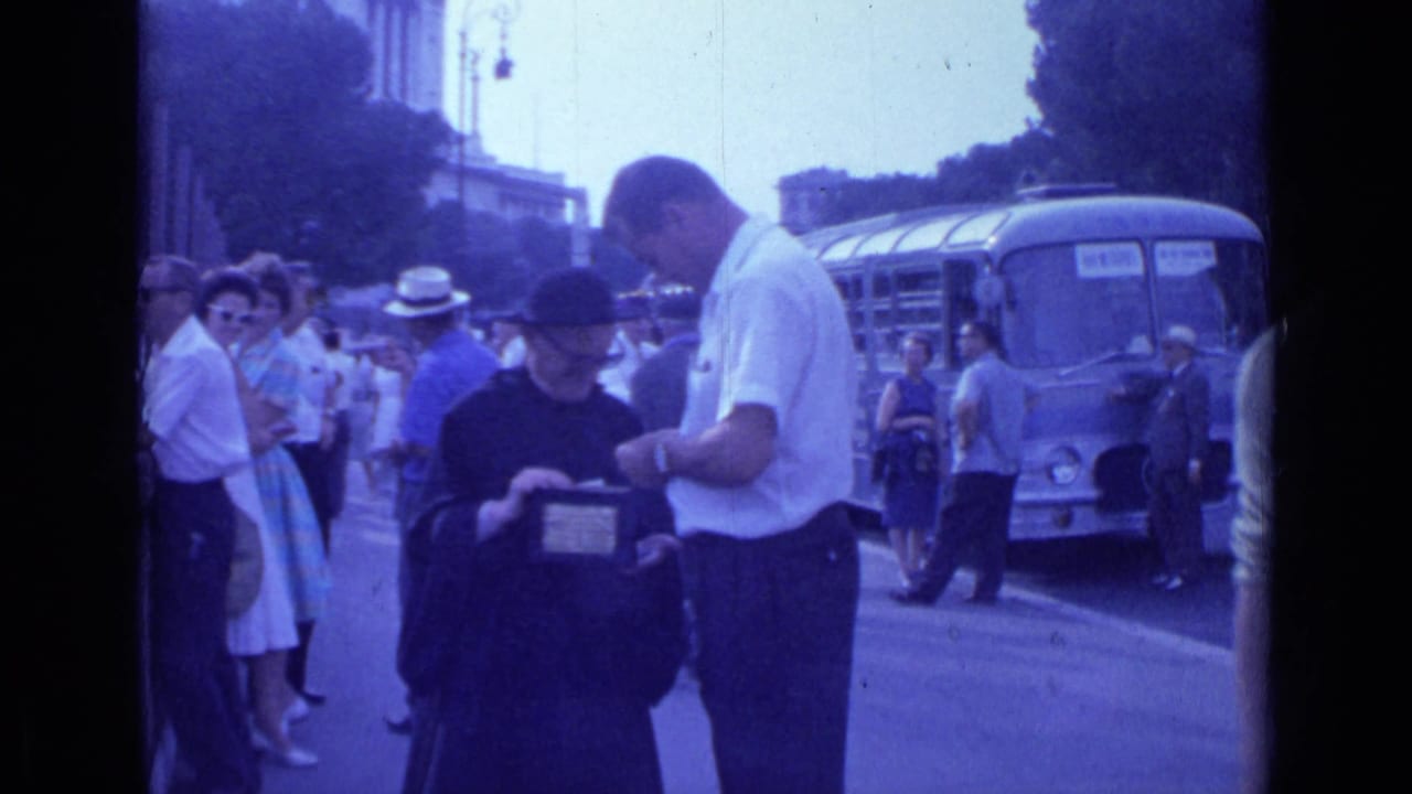 1962 Rome street scene with a priest in black, a man in a white shirt, tourists nearby, and a blue bus in the background.