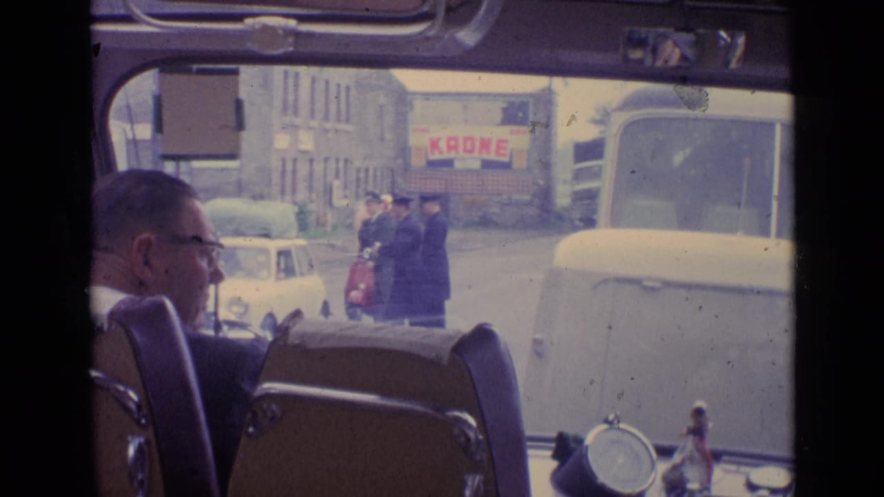 Man in glasses seated inside a vehicle while a street scene is visible through the windshield.