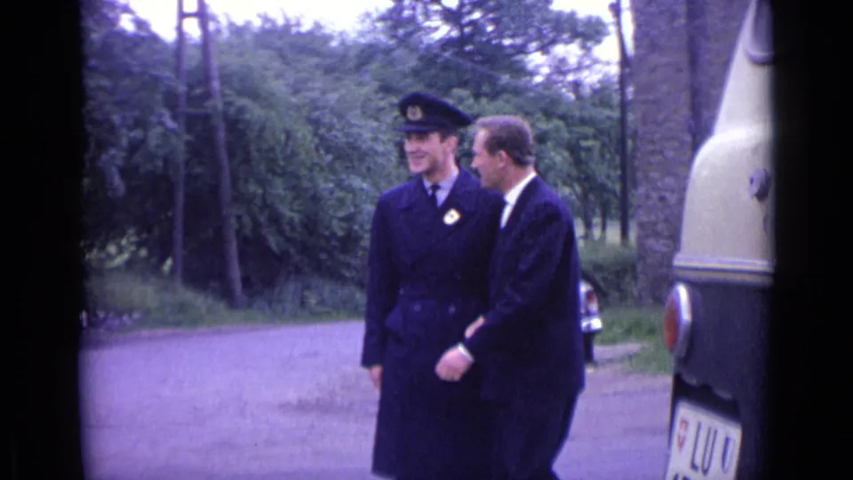The officer and civilian continue together near the roadside, with trees and part of a large cream vehicle visible in the frame.