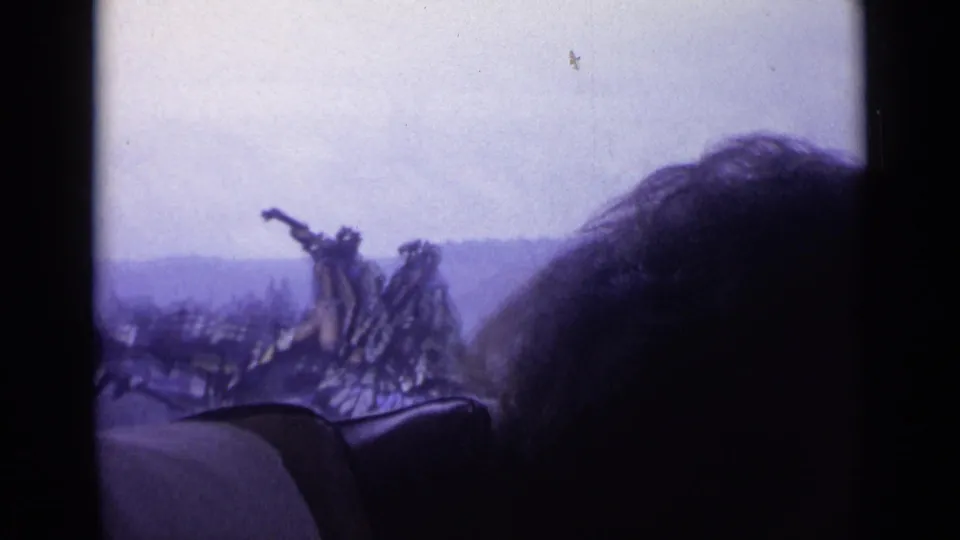 From inside a moving vehicle, the 1962 Swiss footage glimpses a distant monument beyond a window and a dark passenger silhouette.