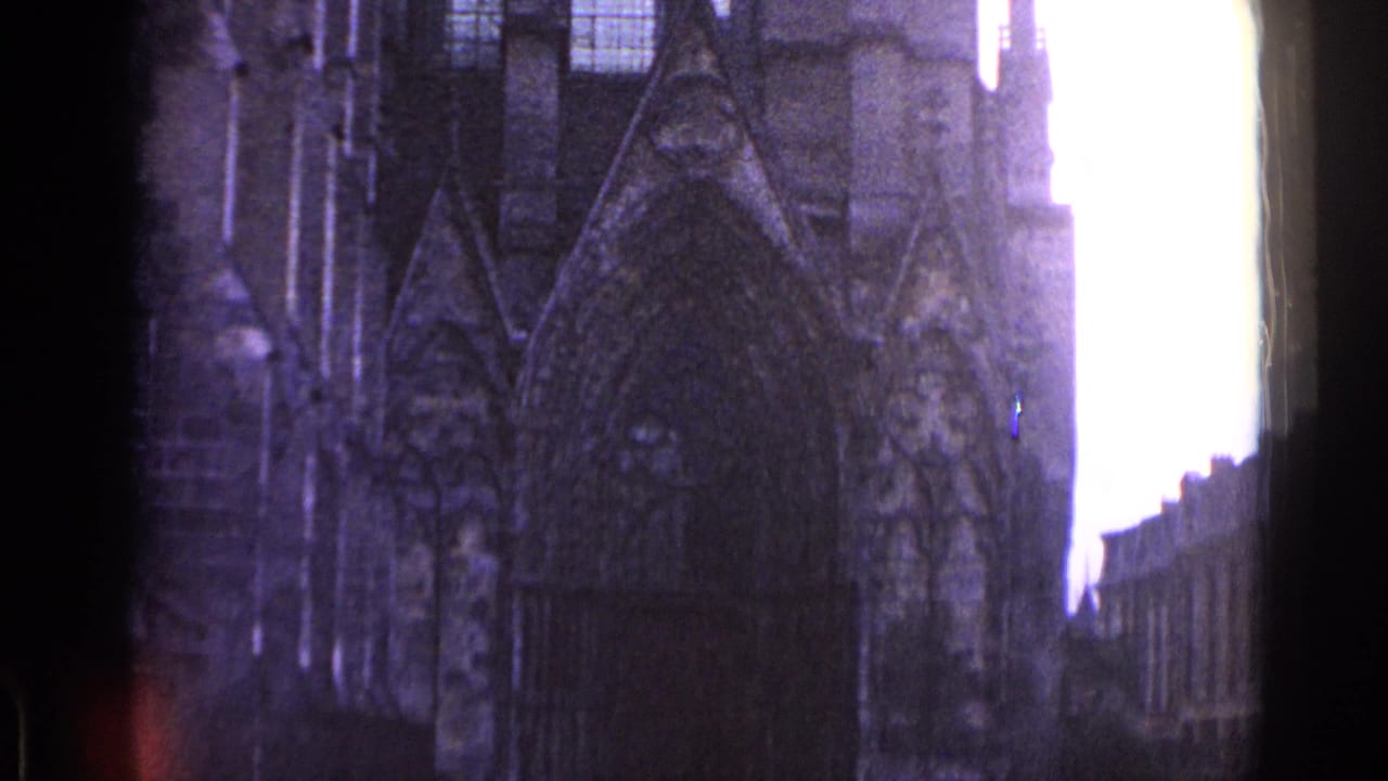 1962 Switzerland 8mm frame showing a shadowed Gothic-style stone facade, possibly a church, filmed from street level.