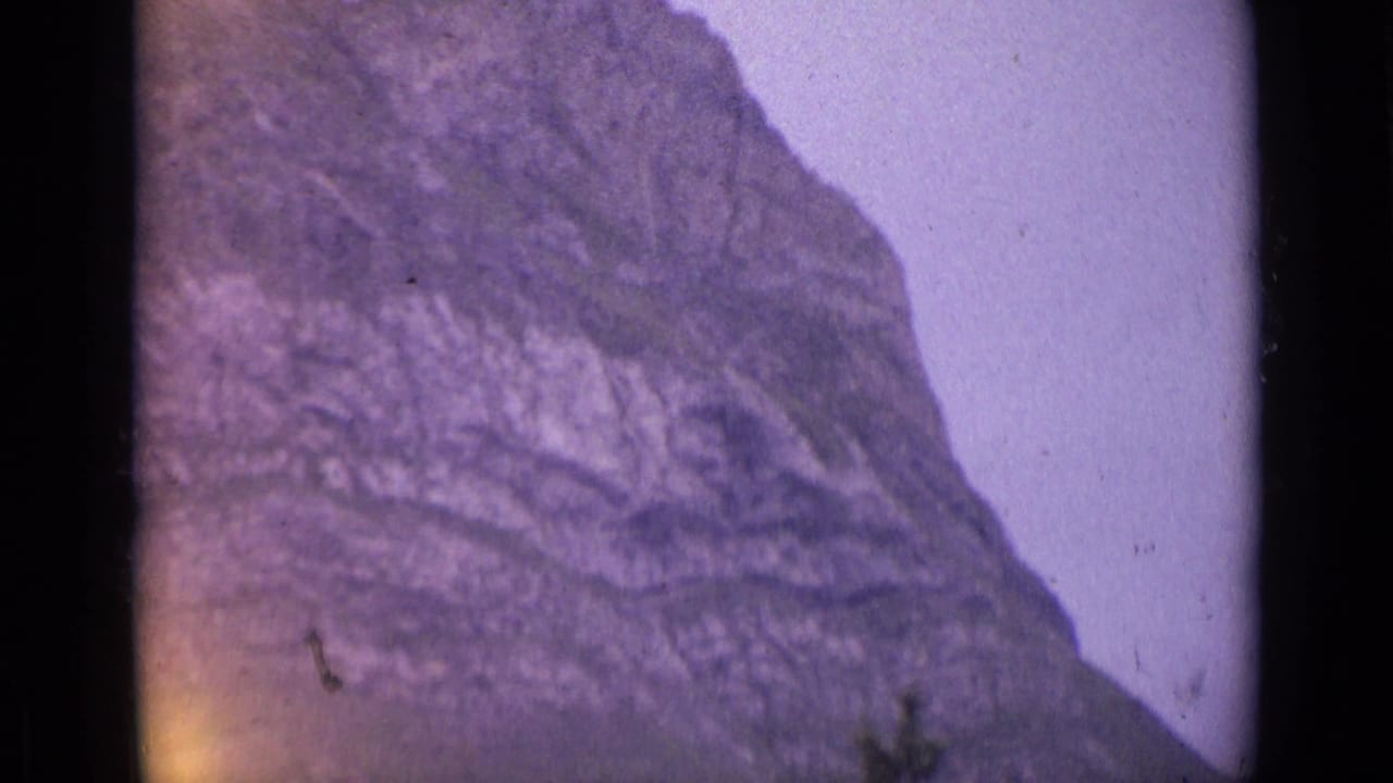 1962 Switzerland 8mm frame of a rugged mountain cliff face with soft purple color shift and visible film grain.