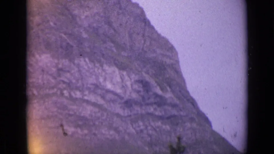 1962 Switzerland 8mm frame of a rugged mountain cliff face with soft purple color shift and visible film grain.