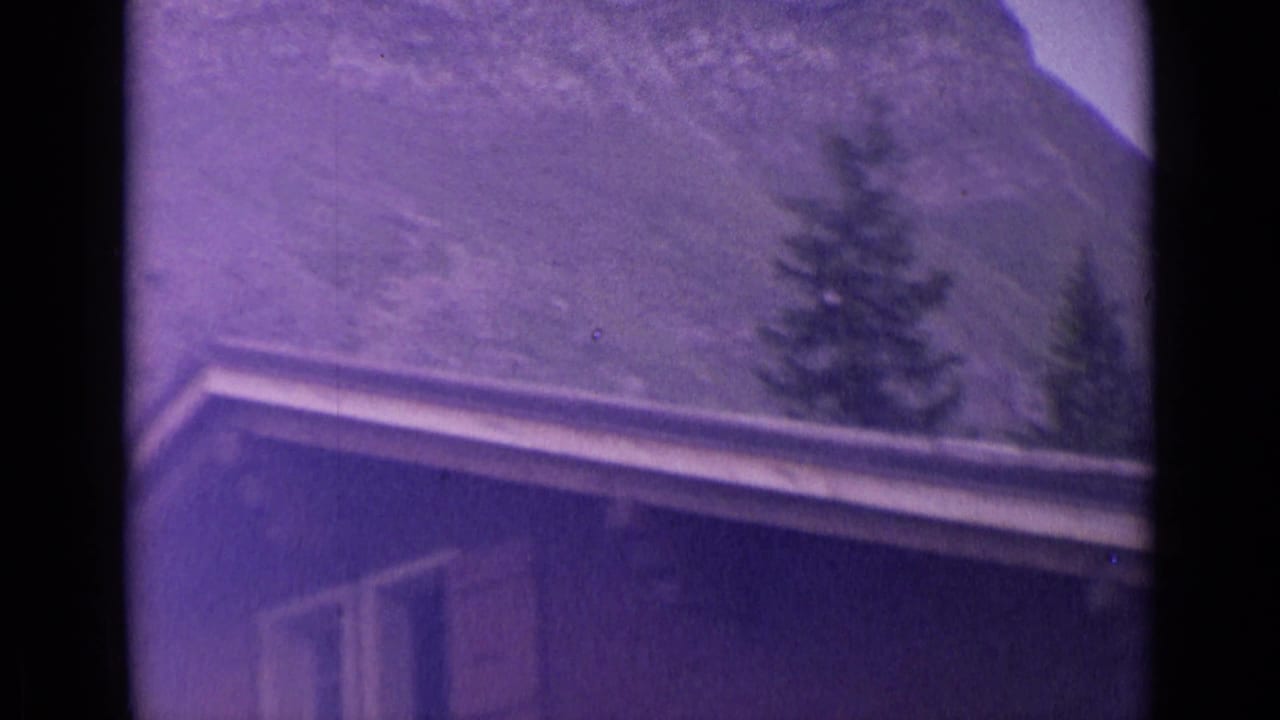 1962 Switzerland 8mm frame showing a building roofline and evergreen trees against a steep alpine slope.