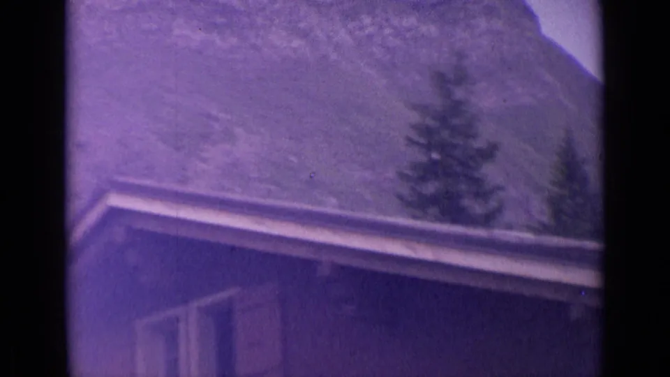 1962 Switzerland 8mm frame showing a building roofline and evergreen trees against a steep alpine slope.