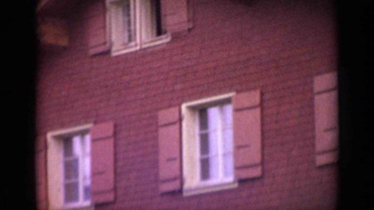 1962 Switzerland 8mm frame showing a red brick house facade with white-framed windows and wooden shutters.