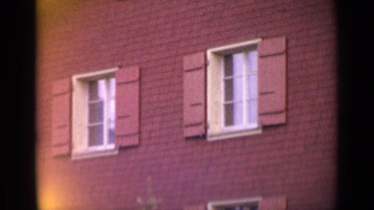 Red brick building with shuttered white-framed windows, partly obscured by dark film borders.