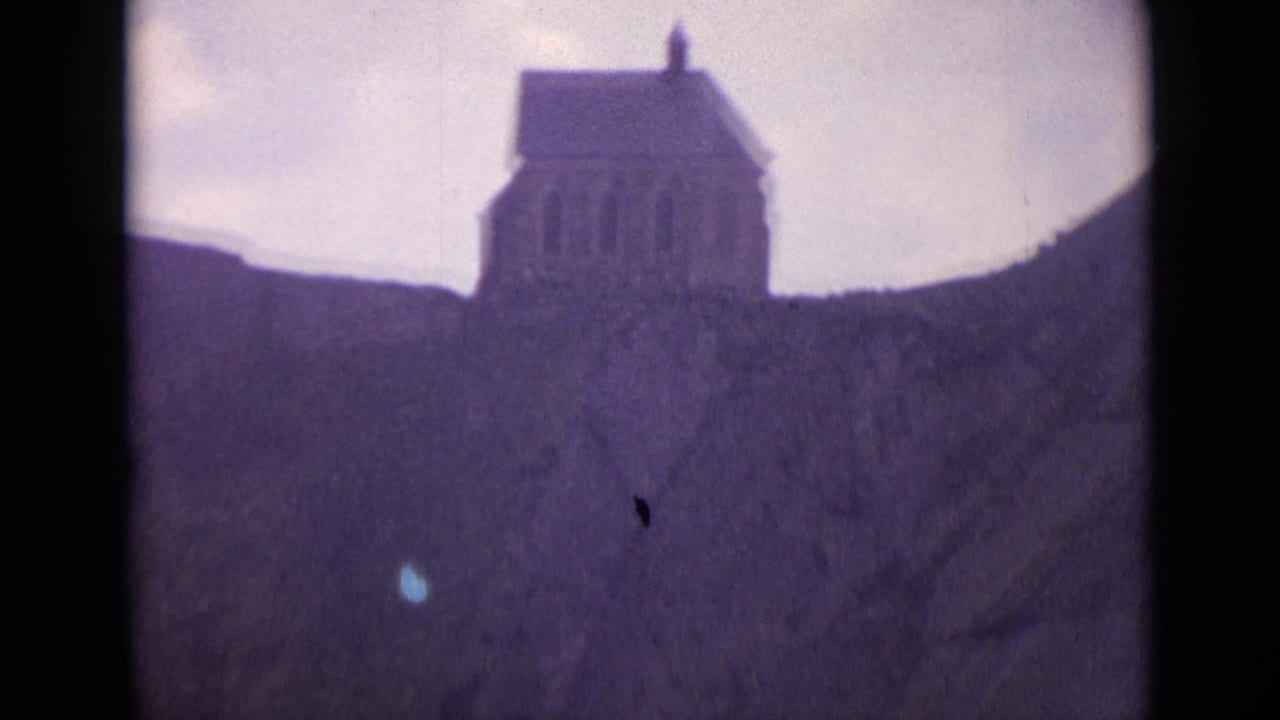1962 Switzerland 8mm frame showing a small chapel-like hillside building with arched openings under a pale cloudy sky.