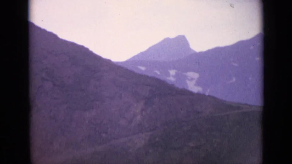 1962 Swiss alpine view with a dark foreground slope, distant peak, and small snowfields in soft 8mm focus.