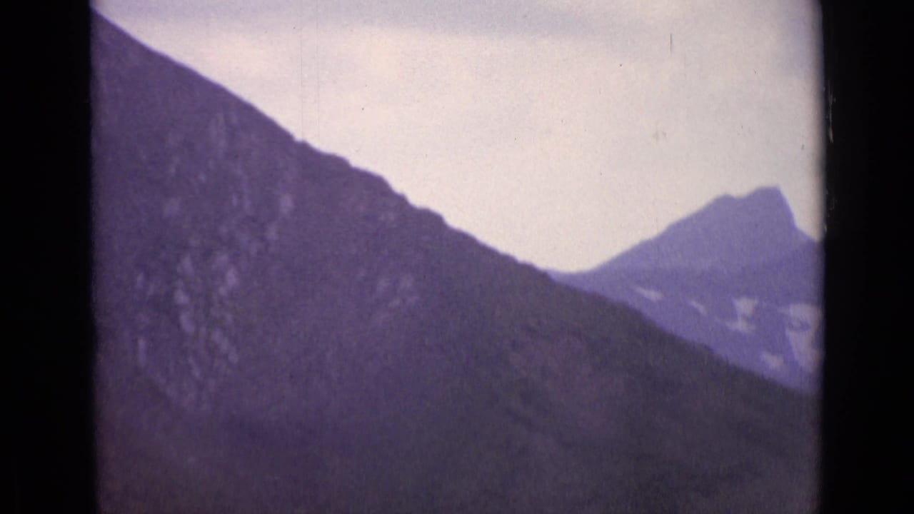 Dark mountain slope beneath a pale sky with a distant peak visible through 8mm frame edges.