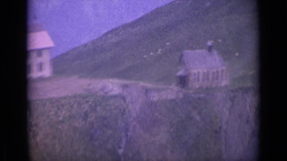 1962 Switzerland 8mm frame of hillside buildings, including a white house and church-like structure, set against alpine slopes.
