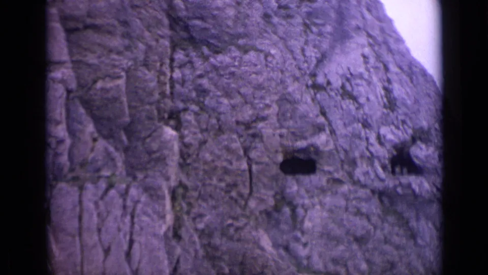 1962 Switzerland frame focused on a craggy mountain rock face, showing dark crevices and a bright sky edge.