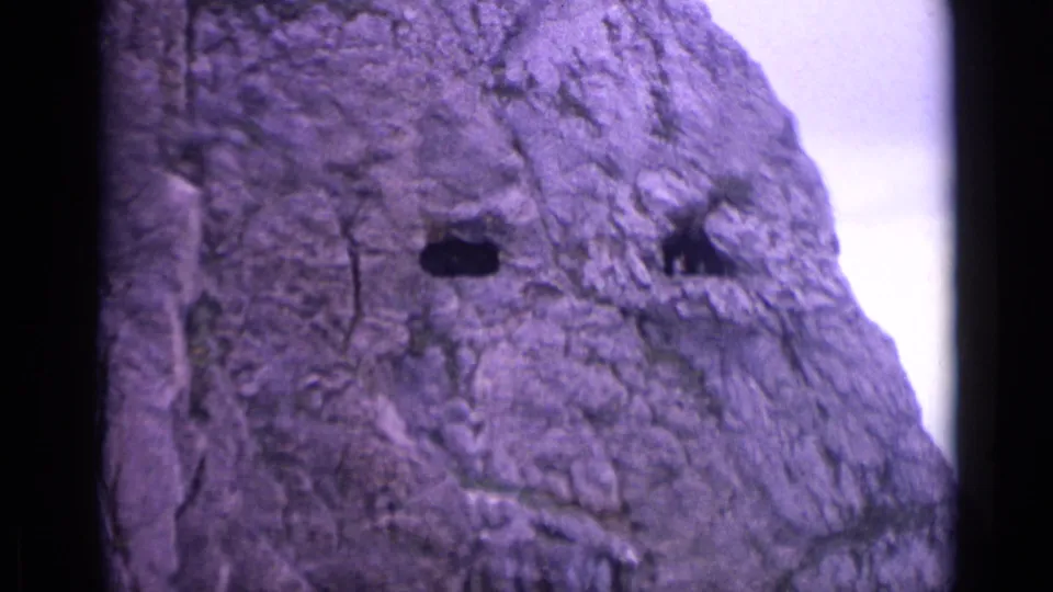 Close mountain rock detail from a 1962 Switzerland home movie, framed tightly with dark crevices and pale sky.