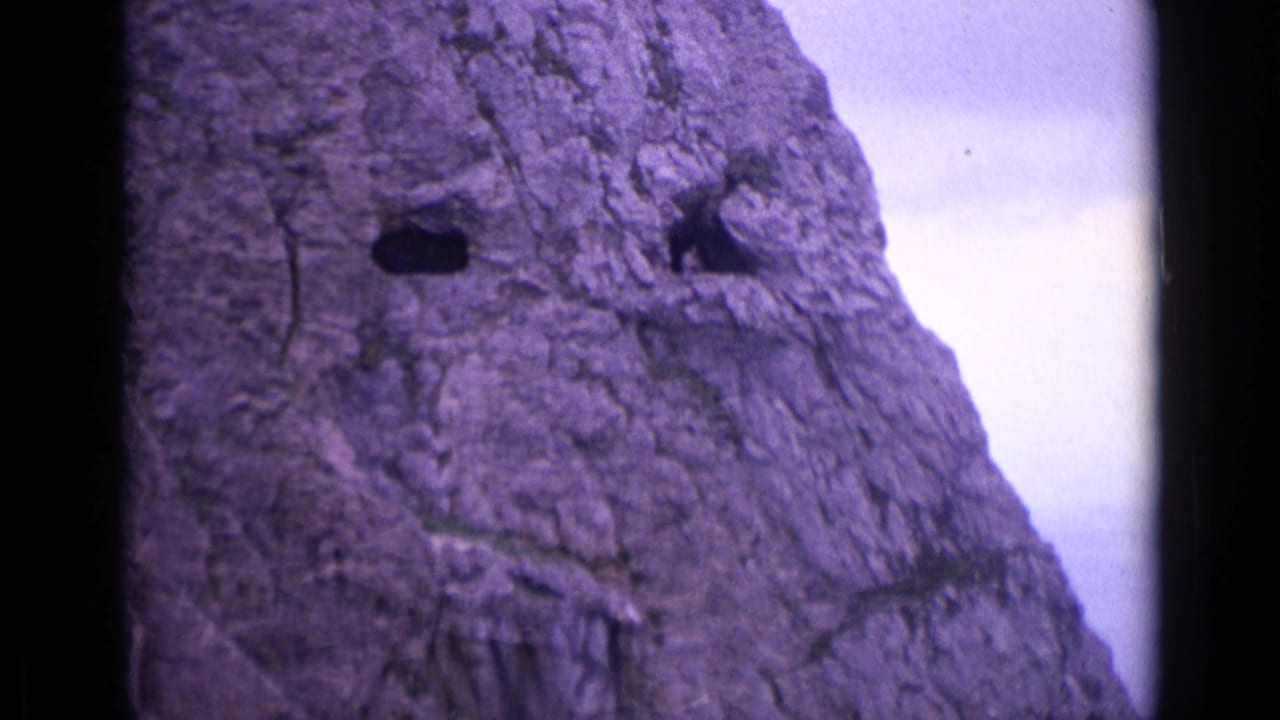 Close view of a rugged rock face with dark openings and pale sky at the edge.