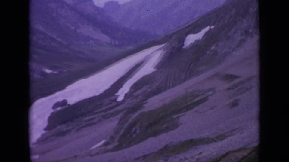 Wide Swiss mountain view on 8mm film, showing snow-dappled alpine slopes and distant hazy peaks.