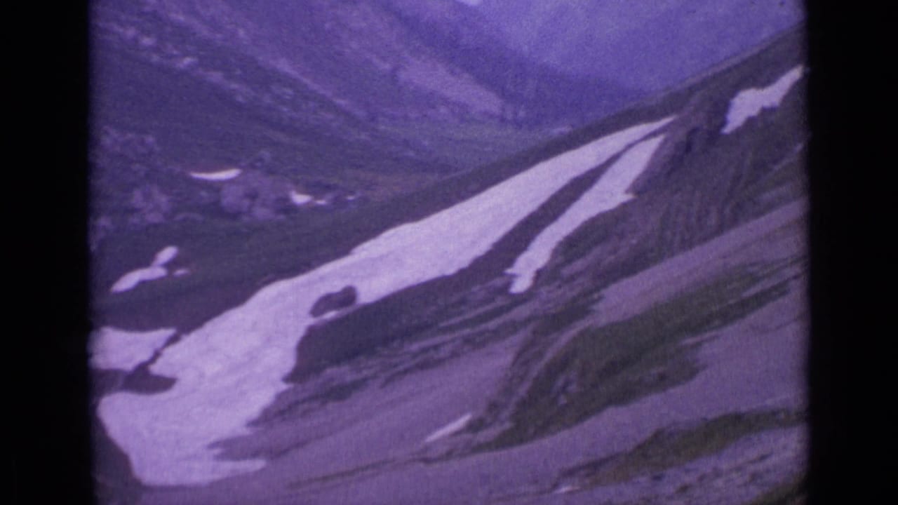 Snow-streaked rocky mountain slope seen through a purple-tinted 8mm frame.