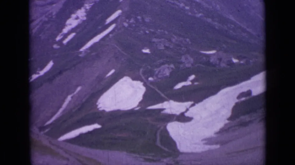1962 Swiss alpine view with rugged ridges, scattered snowfields, and visible 8mm frame edges.