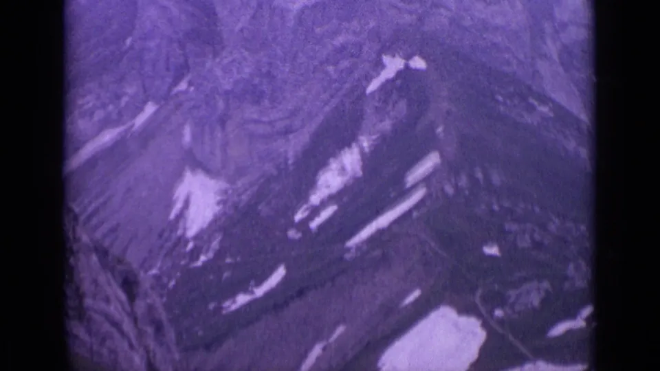 Vintage 8mm Switzerland frame showing a steep rocky mountain slope marked by small snow patches.