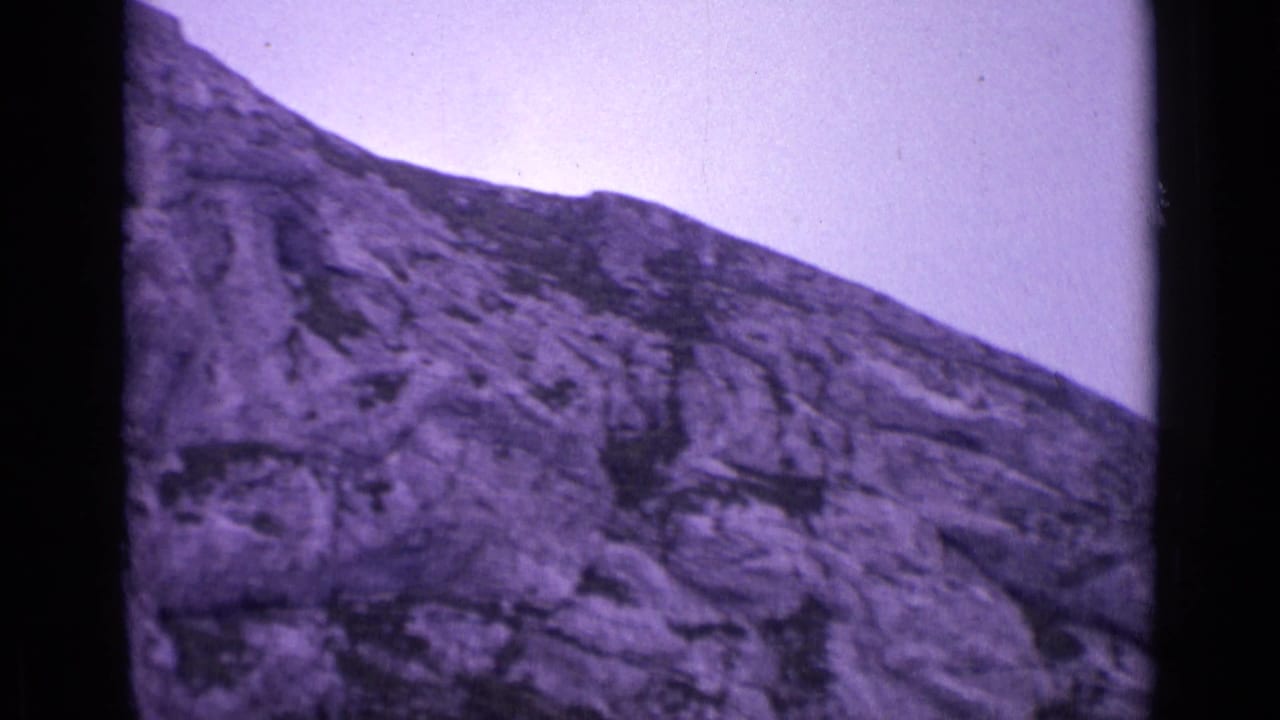 1962 Swiss mountain footage frames a textured rock face with purple color drift and heavy 8mm grain.